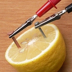 Měděný a pozinkovaný hřebík zabodnuté do citrónu. Digitální multimetr měří napětí mezi hřebíky.